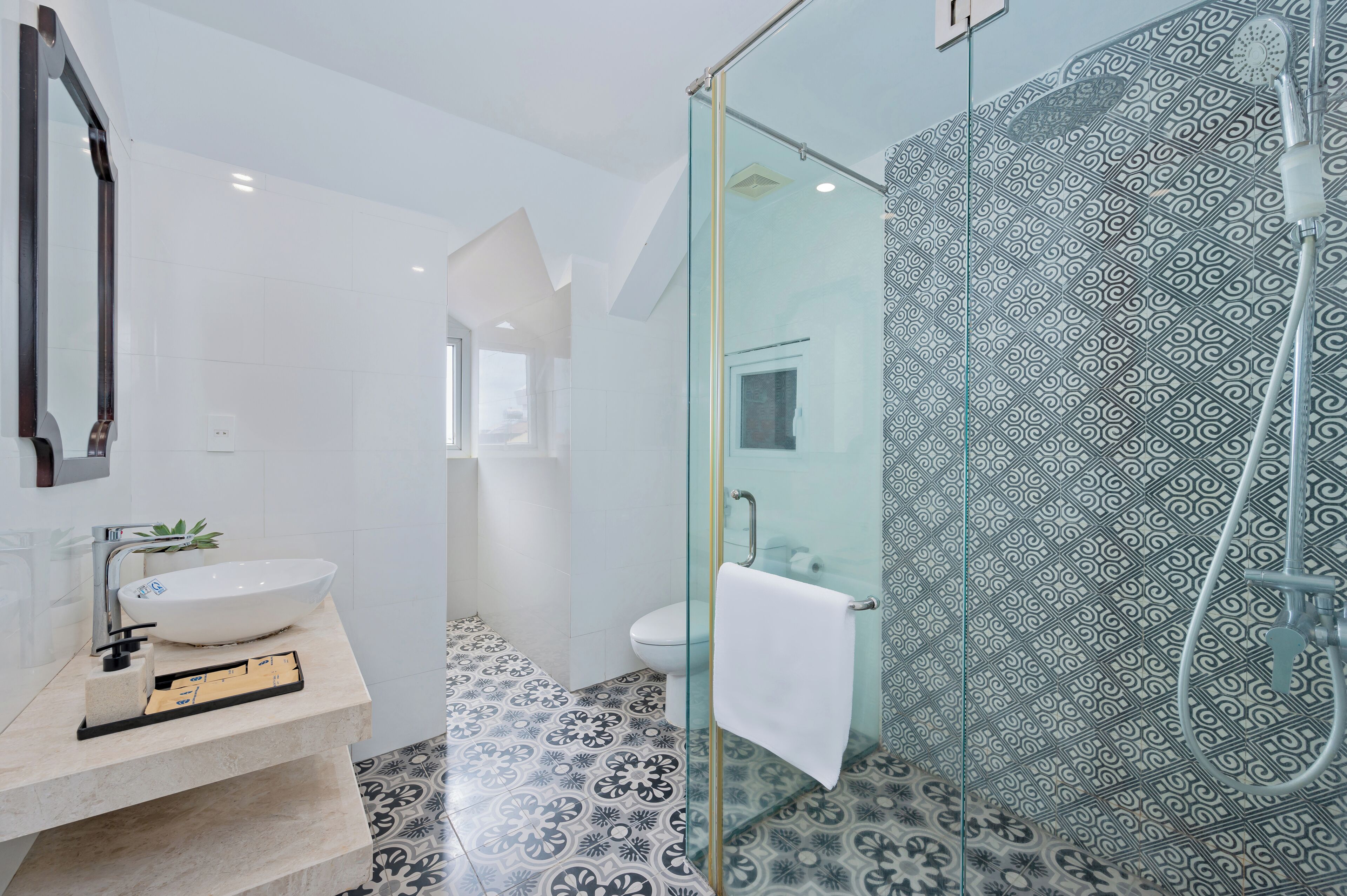 A modern bathroom with a glass shower enclosure, a white sink, and patterned floor tiles.