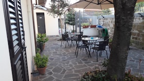 Un patio con suelo de piedra, mobiliario exterior, plantas en macetas y una reja de metal.
