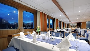 A dining area with tables set for service, large windows, and a view of the evening sky.