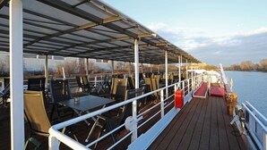 A covered outdoor dining area with tables and chairs, overlooking a body of water.