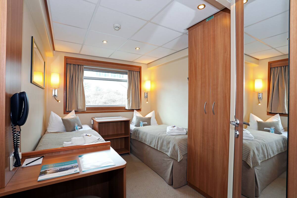 A hotel room with two beds, a desk, a telephone, and a window with curtains.