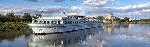 A riverboat with a covered deck and a white and blue color scheme. - Hotelkabinenschiff Junker Jörg (Lutherstadt Wittenberg)