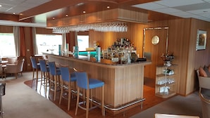 A bar area with a wooden bar counter, blue bar stools, and a variety of bottles and glasses.