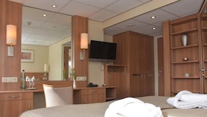 A hotel room with a bed, a desk, a chair, a TV, and a wardrobe.