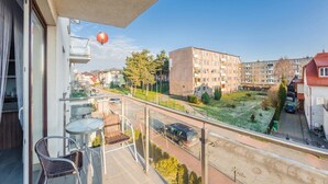 A balcony with a glass railing overlooking a residential area, featuring a clear view of buildings and a road. - Family Homes - Apartamenty Bursztynowe (Wladyslawowo)