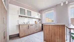 A modern kitchen with white cabinets, a wooden island, and a window providing natural light. - Family Homes - Apartamenty Bursztynowe (Wladyslawowo)