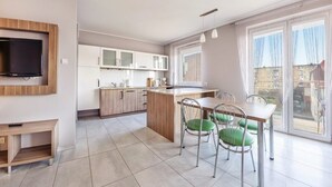 A modern kitchen with a dining area, large windows, and a flat-screen TV mounted on the wall. - Family Homes - Apartamenty Bursztynowe (Wladyslawowo)