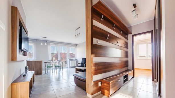 A modern living room with a built-in entertainment unit, a dining area with a table and chairs, and a view of the outside. - Family Homes - Apartamenty Bursztynowe (Wladyslawowo)