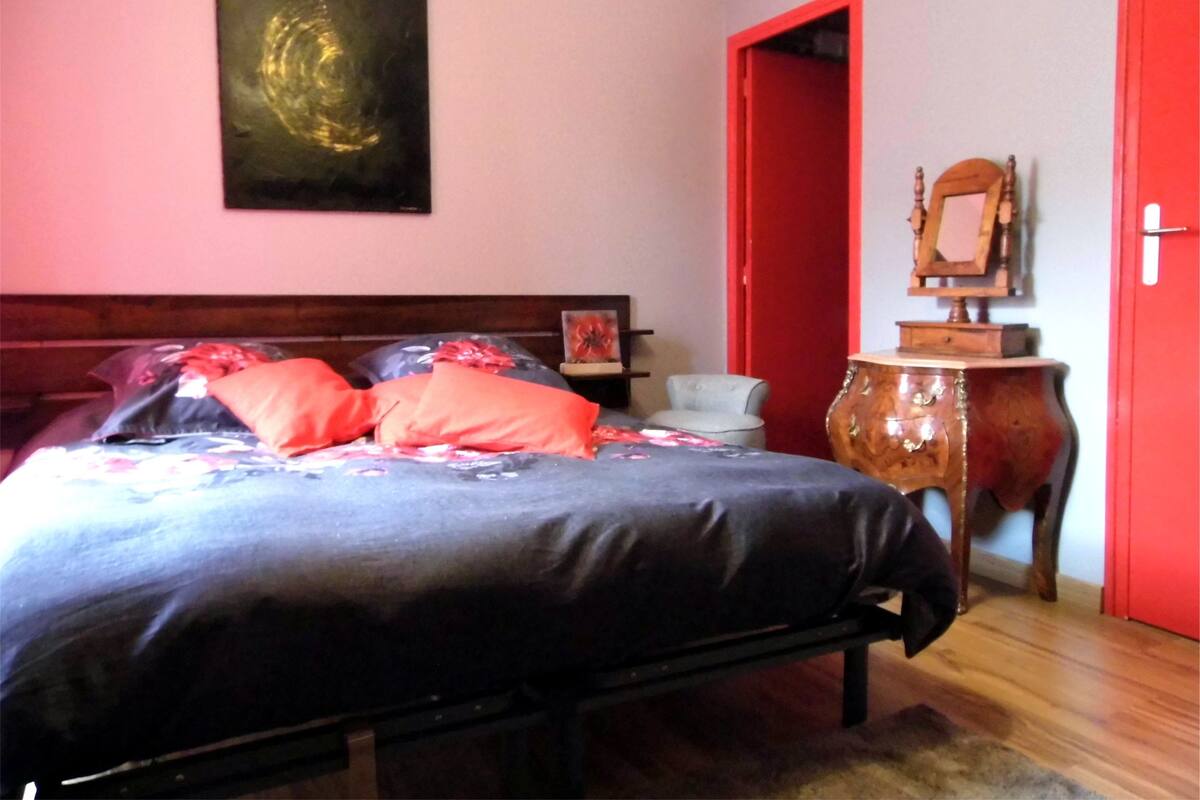 A bedroom with a bed, a wooden headboard, a red door, a wooden cabinet, and a painting on the wall.