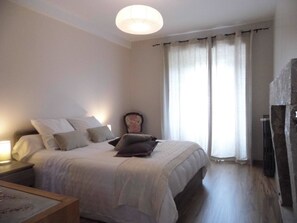 A bedroom with a bed, a nightstand, a chair, and a large window with curtains. - L'Atelier S (Mont Lozere et Goulet)