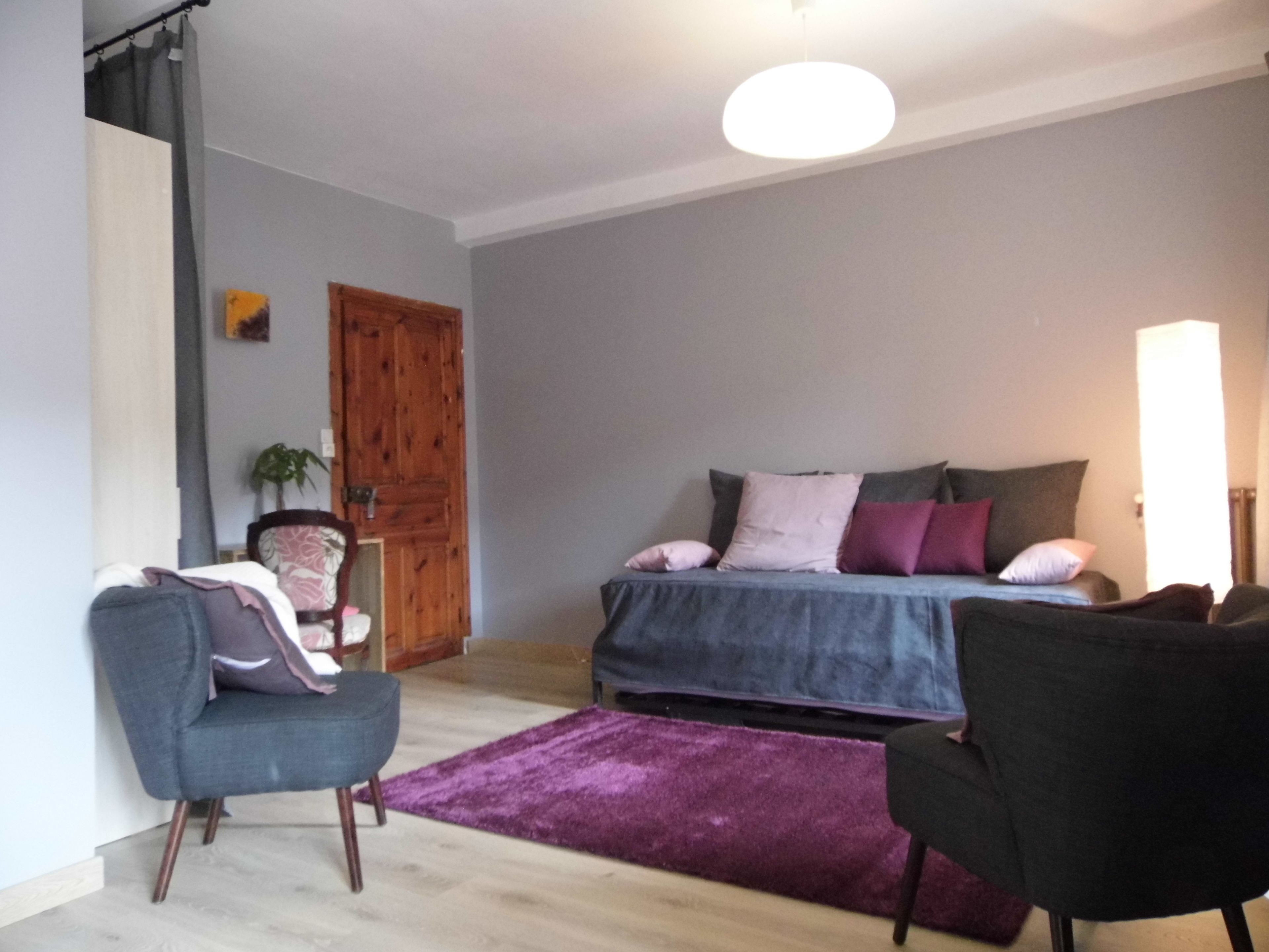 Ein Schlafzimmer mit einem Bett, zwei Stühlen, einer Holztür und einem violetten Teppich.