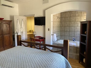 A bedroom with a bed, a desk, a chair, a TV, a bathroom with a shower, and a cabinet.