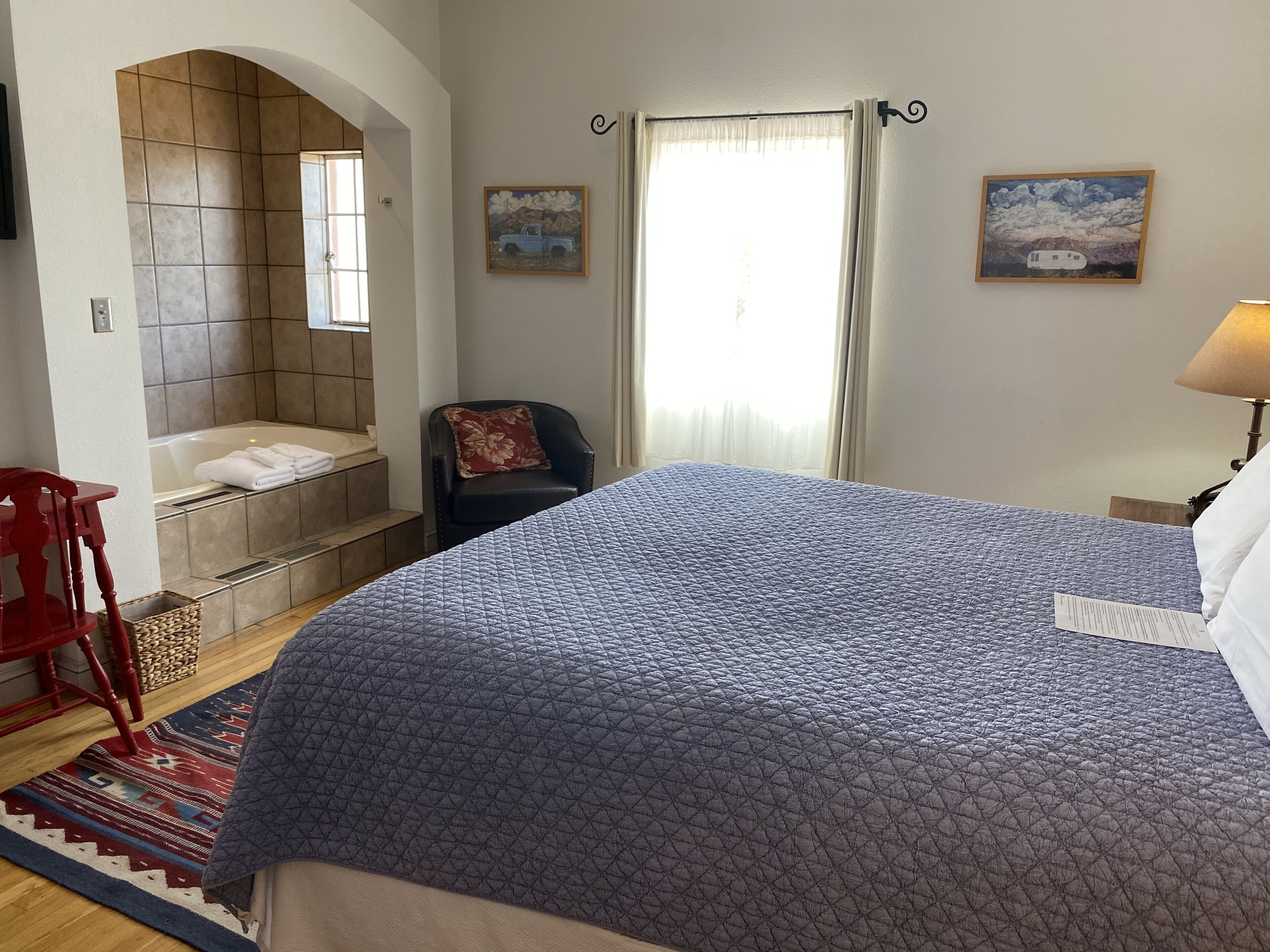 Un dormitorio con una cama grande, un baño con bañera, una silla y dos cuadros en la pared.