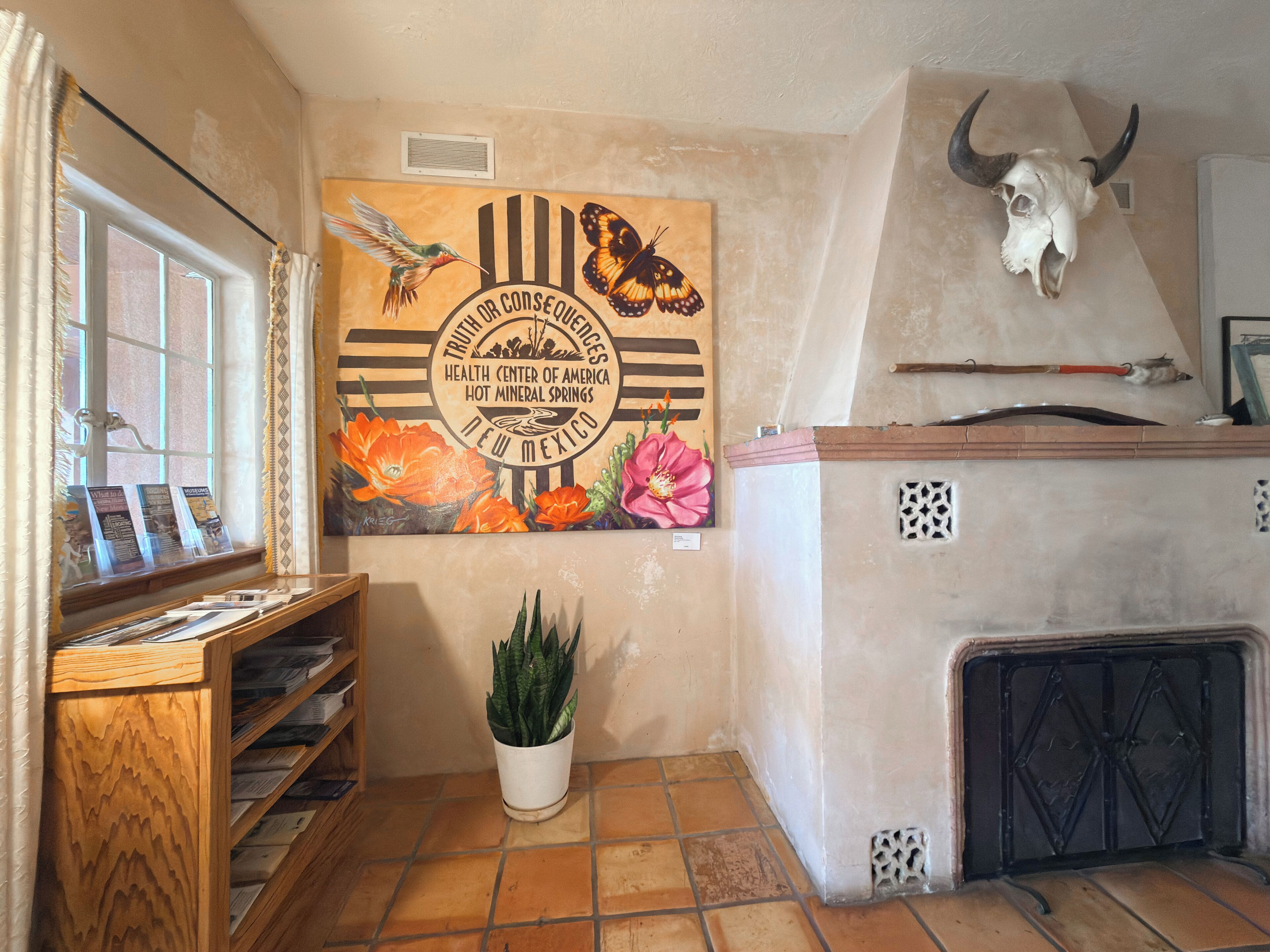 A room with a mural of butterflies and flowers, a wooden shelf with brochures, a potted plant, and a bull skull on the wall.