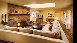 A cozy living room with a stone fireplace, a large sofa, a television, and a dining area. - Sierra Grande, A Ted Turner Retreat (Truth or Consequences)