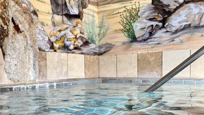 Una piscina interior transparente con un mural de una pared de roca y un borde de piedra.