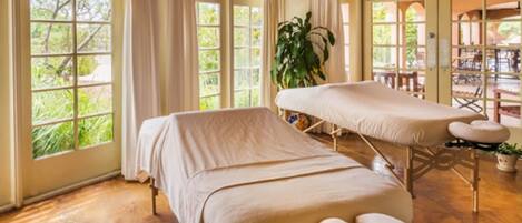 Une pièce dotée de deux tables de massage, de grandes fenêtres avec des rideaux, d’un plafond en bois et offrant une vue sur l’extérieur.