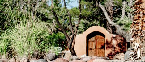 Un edificio rústico con una entrada en arco, rodeado de rocas y vegetación escasa.
