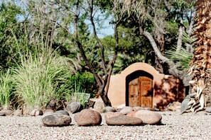 A rustic building with an arched entrance, surrounded by rocks and sparse vegetation. - Sierra Grande, A Ted Turner Retreat (Truth or Consequences)