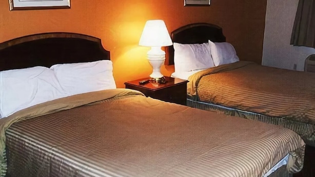 A hotel room with two beds, each with a headboard, a bedside table with a lamp, and a framed picture on the wall. - A Victory Inn East Dearborn (Detroit)