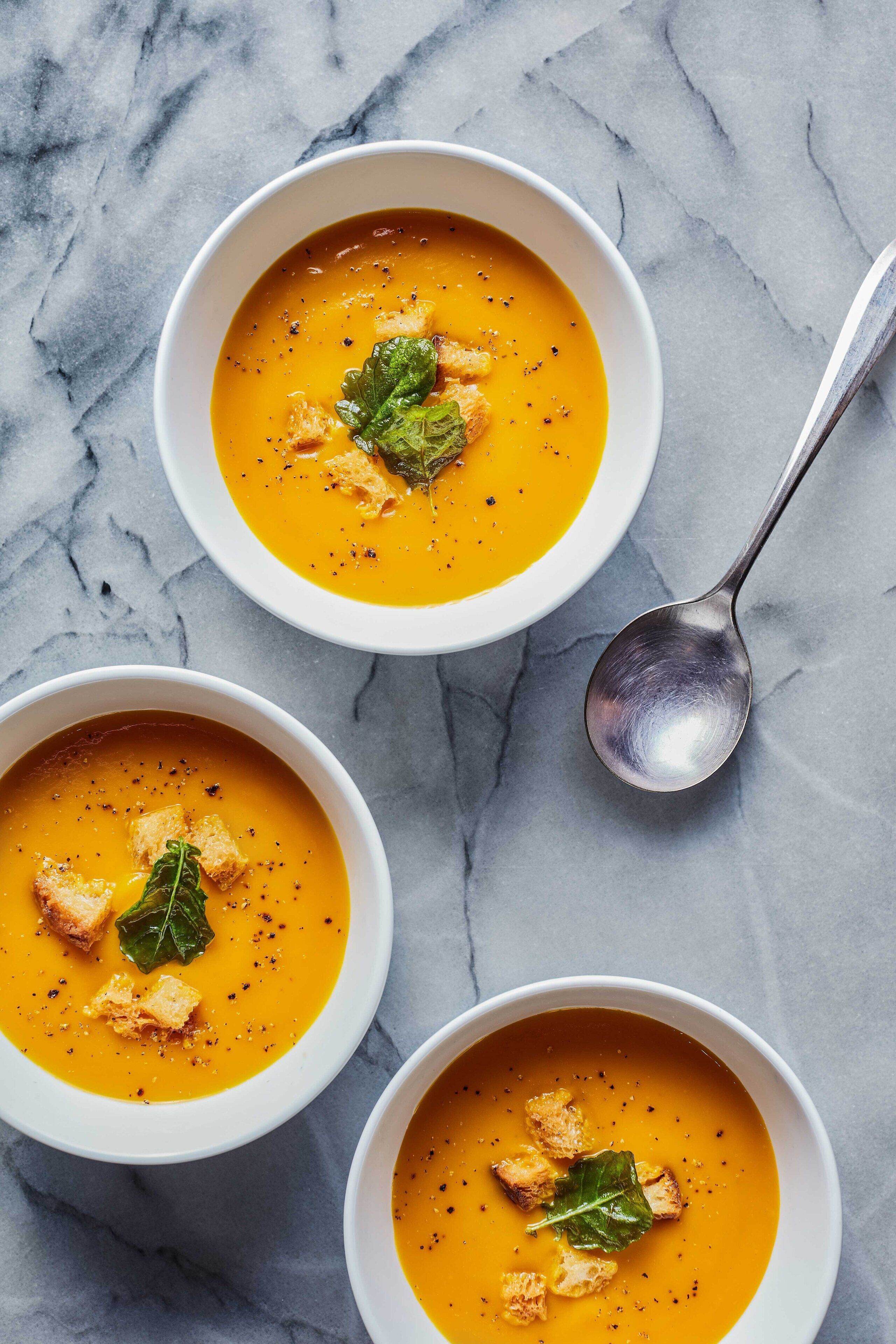 Three bowls of soup with croutons and a leaf garnish on a marble surface.