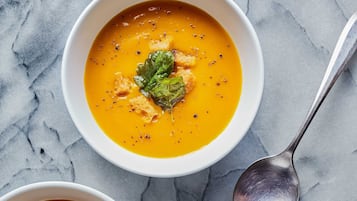 Three bowls of soup with croutons and a leaf garnish on a marble surface.