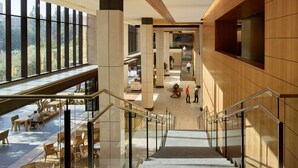 A modern interior with a central staircase, glass railings, and a view of the outdoor area. - Luskin Hotel (Los Angeles)