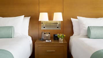 A hotel room with two beds, a bedside table with a lamp, a telephone, and a small vase with flowers.