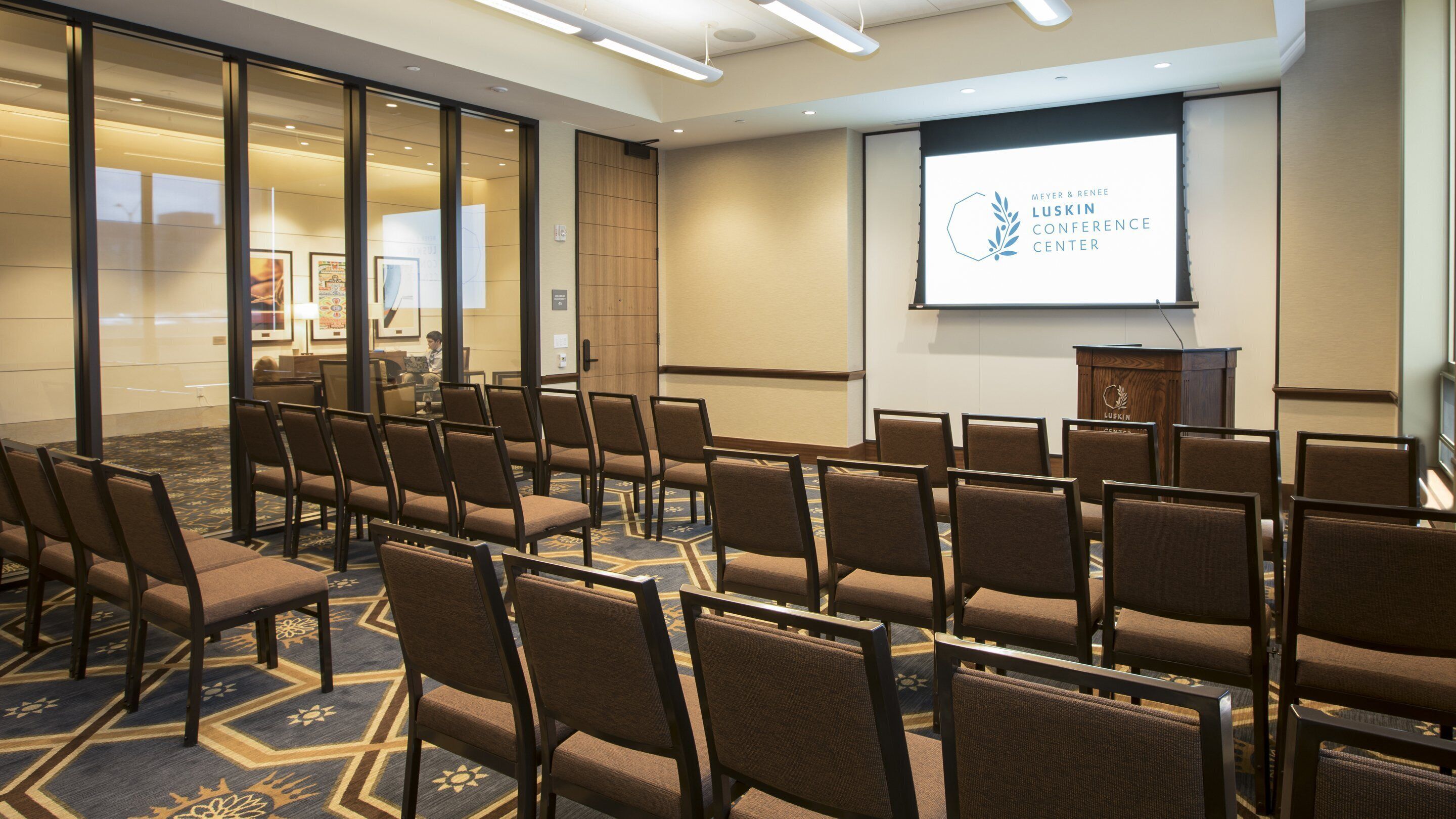 Un salón de conferencias con filas de sillas, un atril y una pantalla para presentaciones.