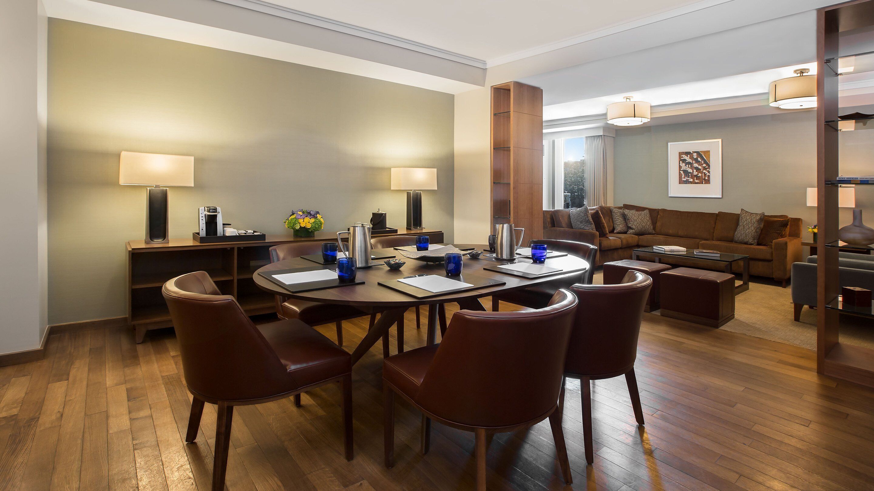 A modern hotel room with a dining area, a sofa set, and a large window.