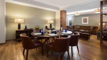 A modern hotel room with a dining area, a sofa set, and a large window.