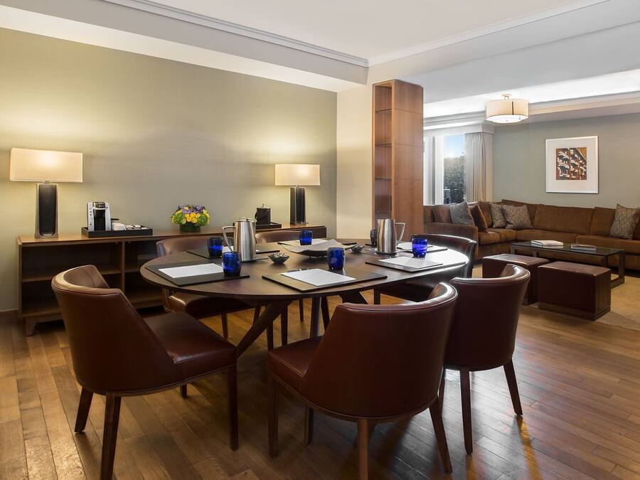 A modern hotel room with a dining area, a sofa set, and a large window.