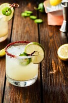 Uma margarita com borda salgada e um toque de limão sobre uma mesa de madeira.