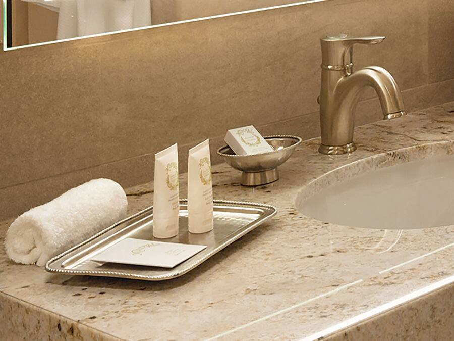A bathroom with a marble countertop, a sink, a mirror, and toiletries on a tray.