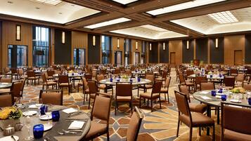 A large banquet hall with multiple round tables, each set with chairs, plates, cutlery, and blue glassware.
