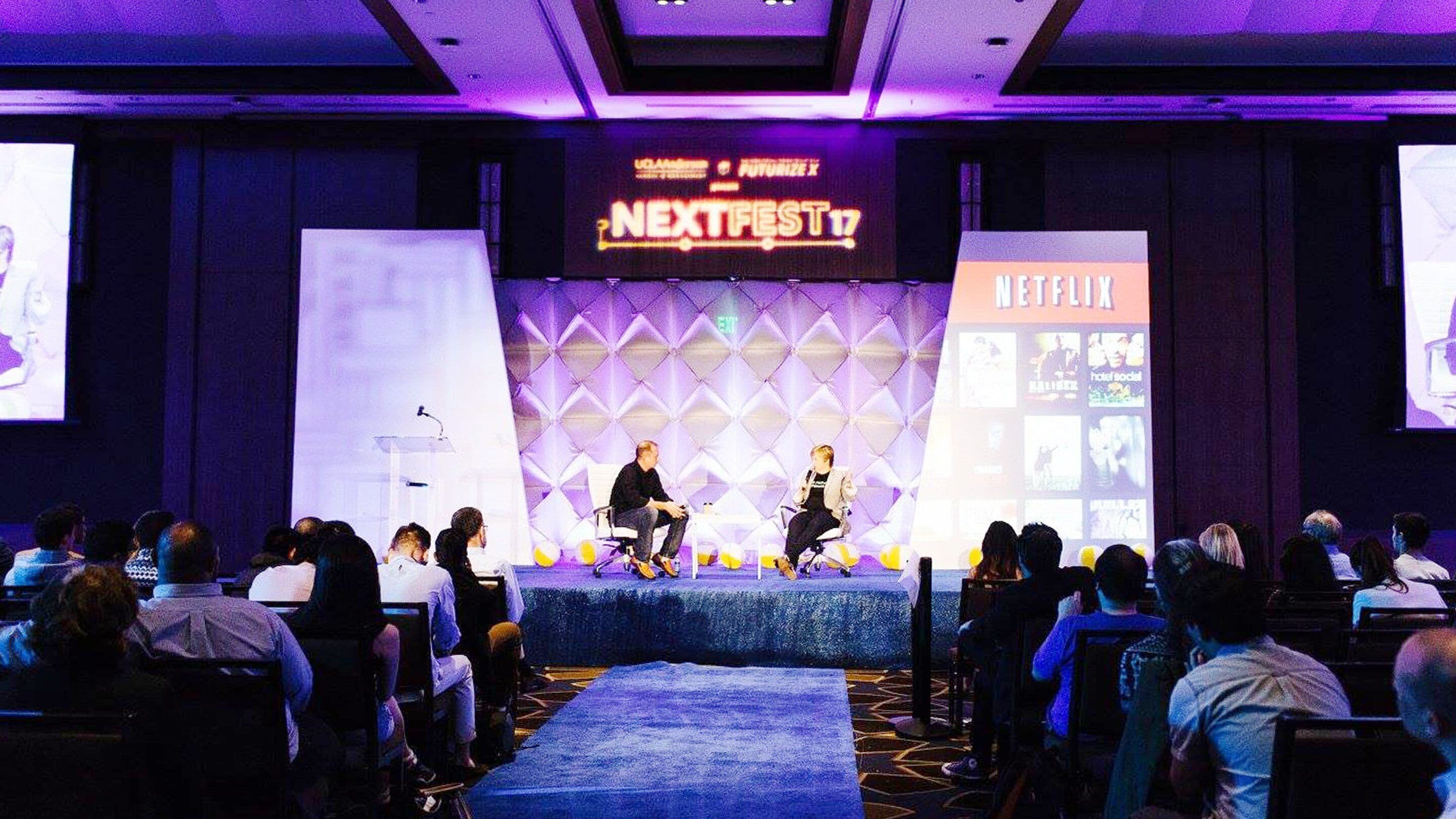 A conference room with a stage for presentations, a large screen displaying 'NEXTFEST 17', and a 'NETFLIX' sign.