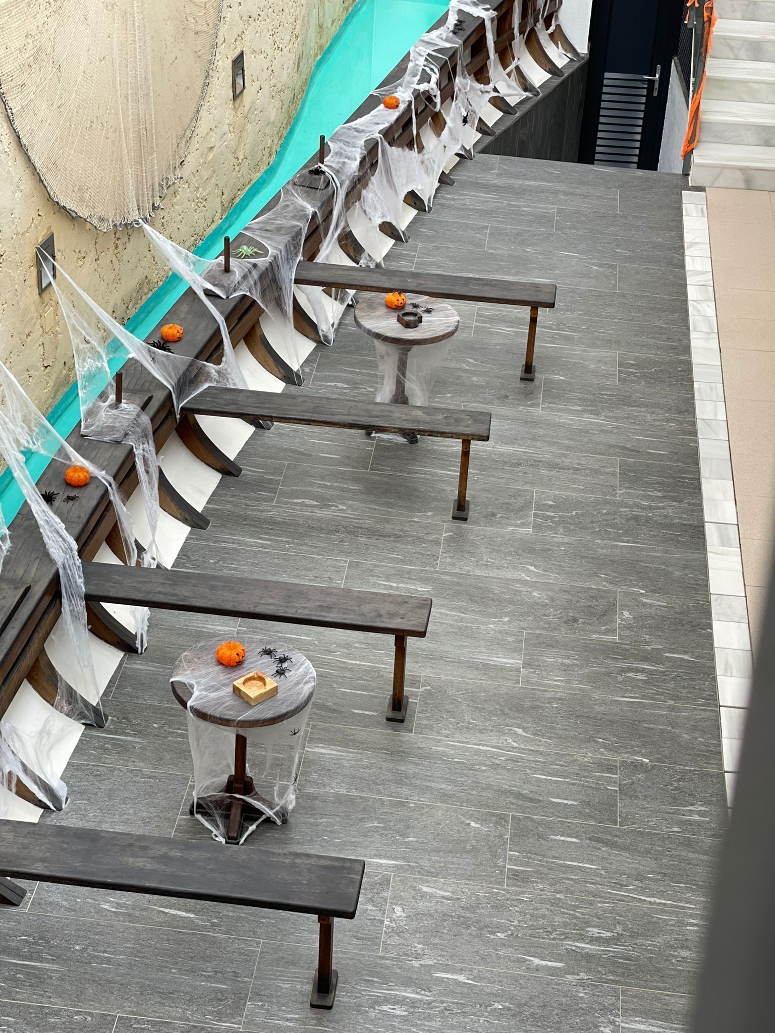 A row of wooden tables with chairs, some covered in plastic and spider webs, suggesting a Halloween theme.