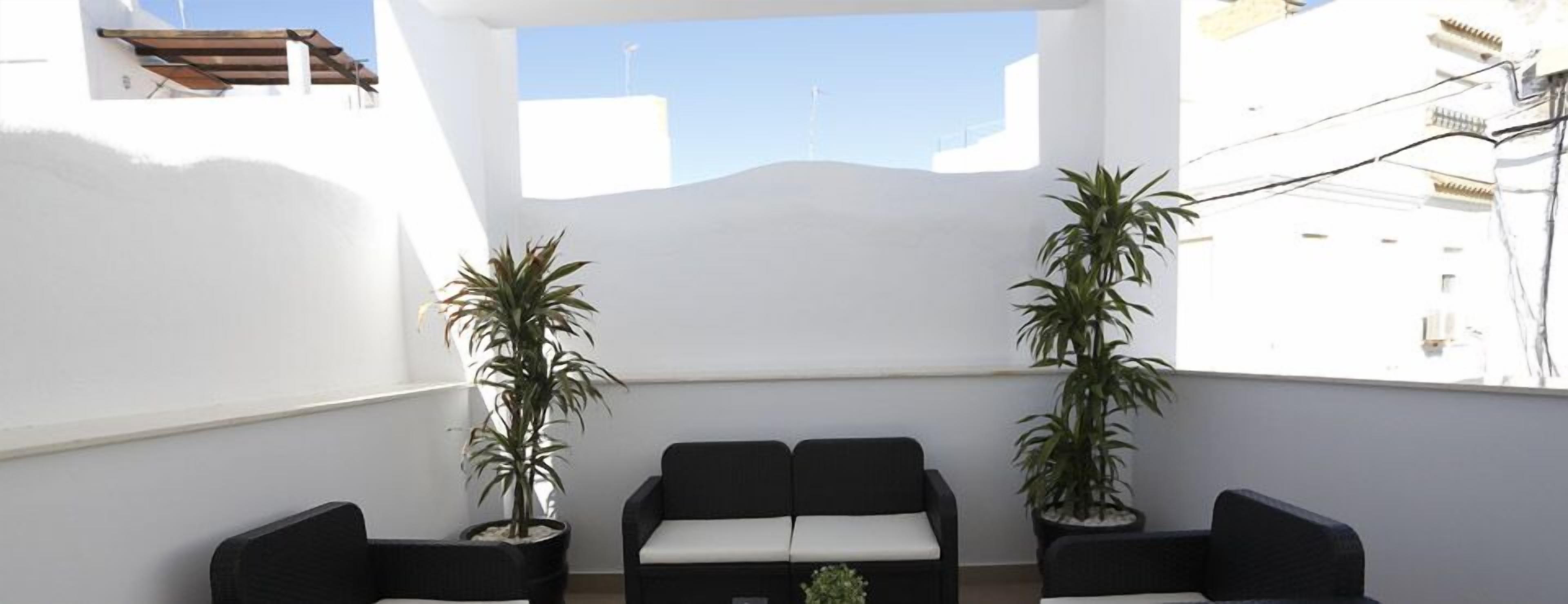 A balcony with a white wall, two potted plants, and a black sofa.