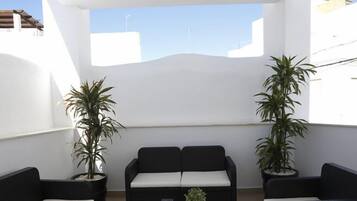 A balcony with a white wall, two potted plants, and a black sofa.