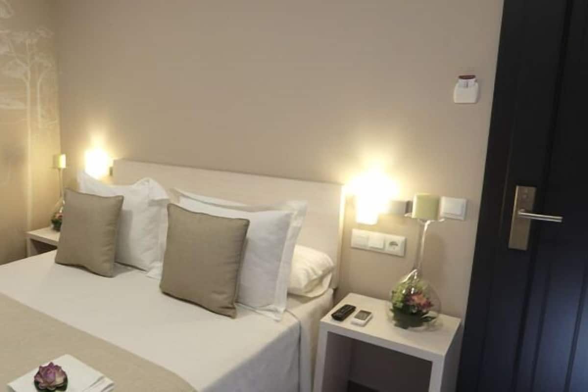 A hotel room with a bed, two bedside tables, and a nightstand with a phone and a small plant.