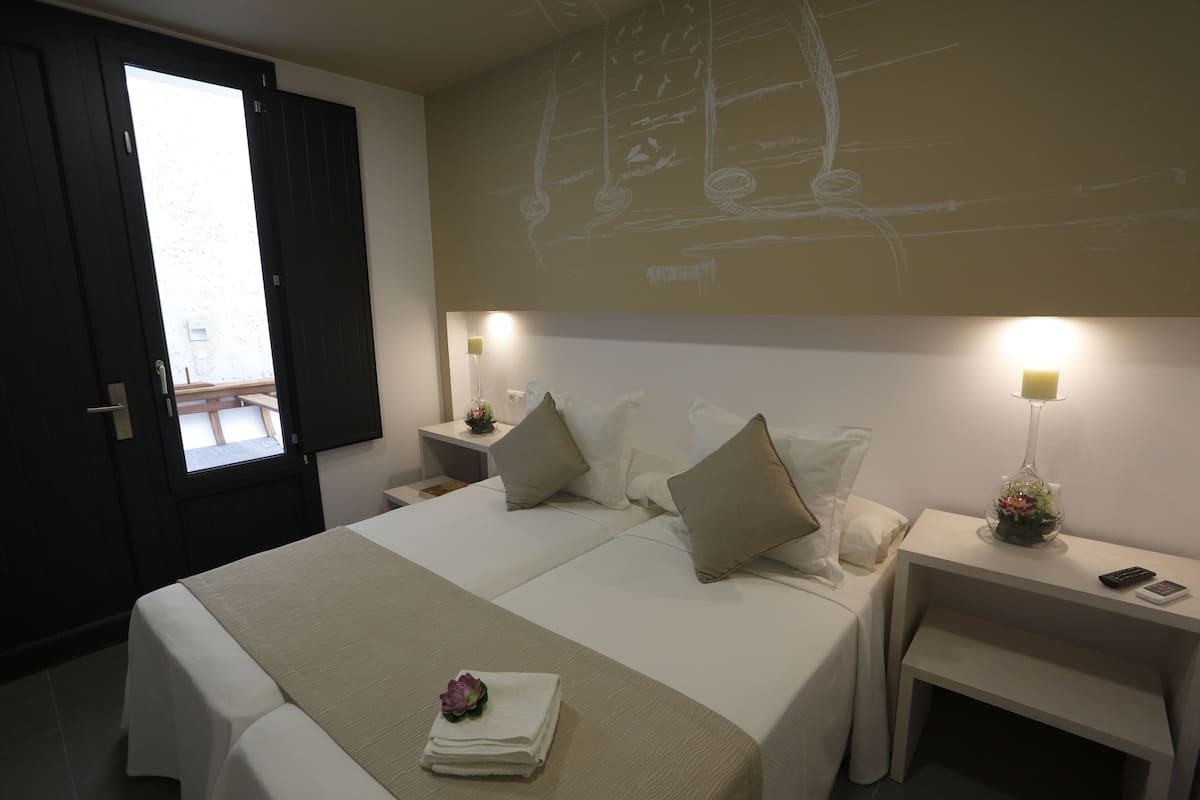 A hotel room with two beds, a desk, bedside tables with lamps, and a large window.