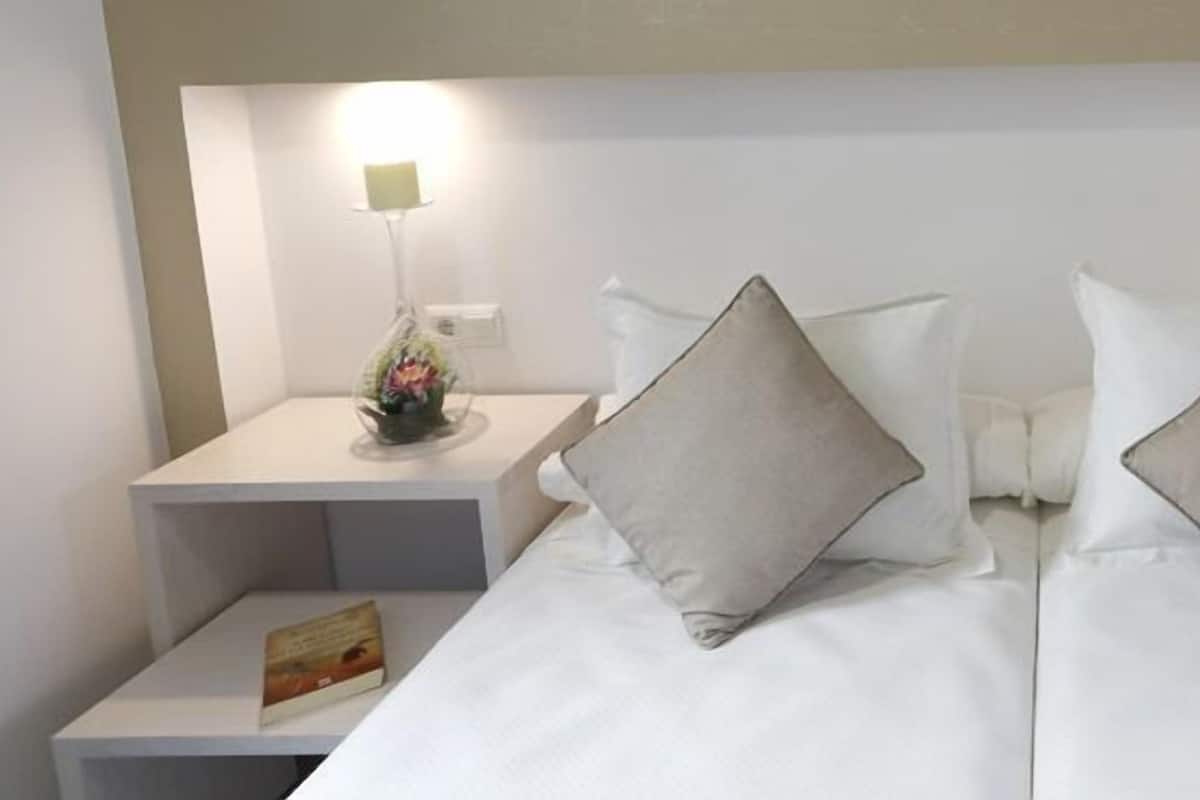 A hotel room with two beds, each with a pillow and a nightstand with a lamp and a vase of flowers.