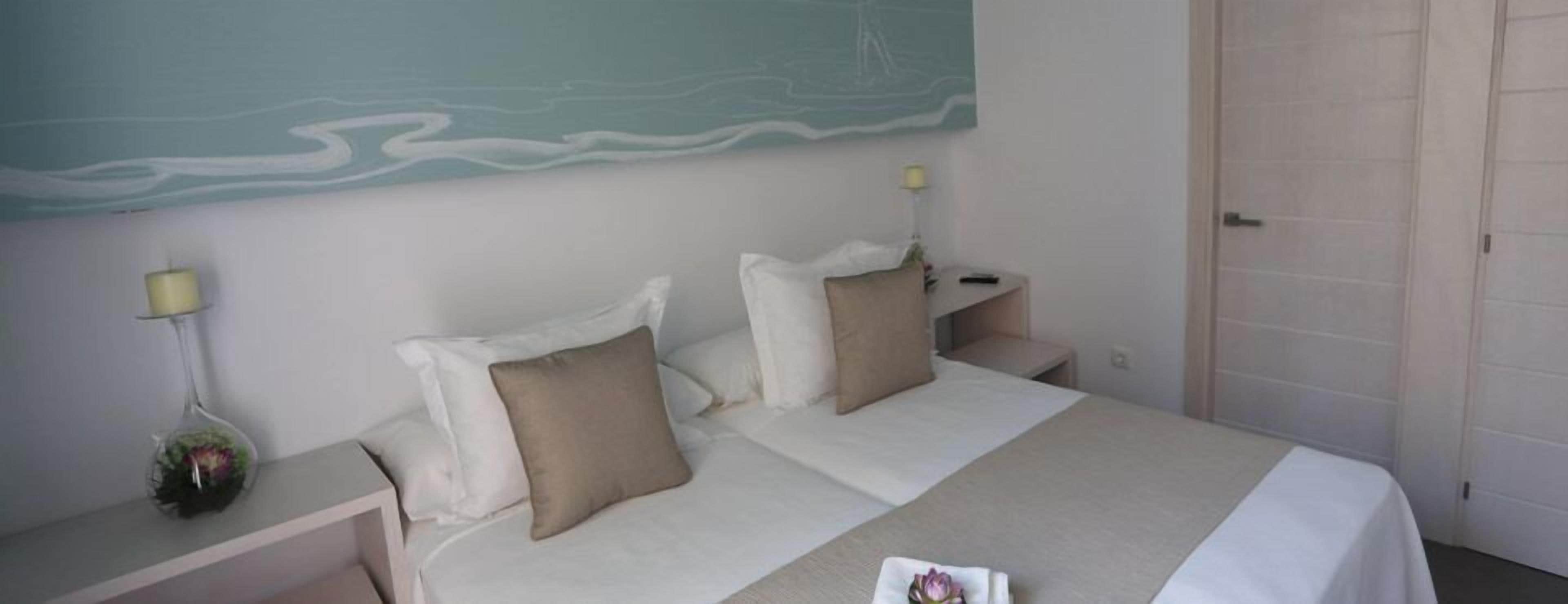 A hotel room with a bed, two bedside tables, a nightstand, a lamp, and a wall with a mural.