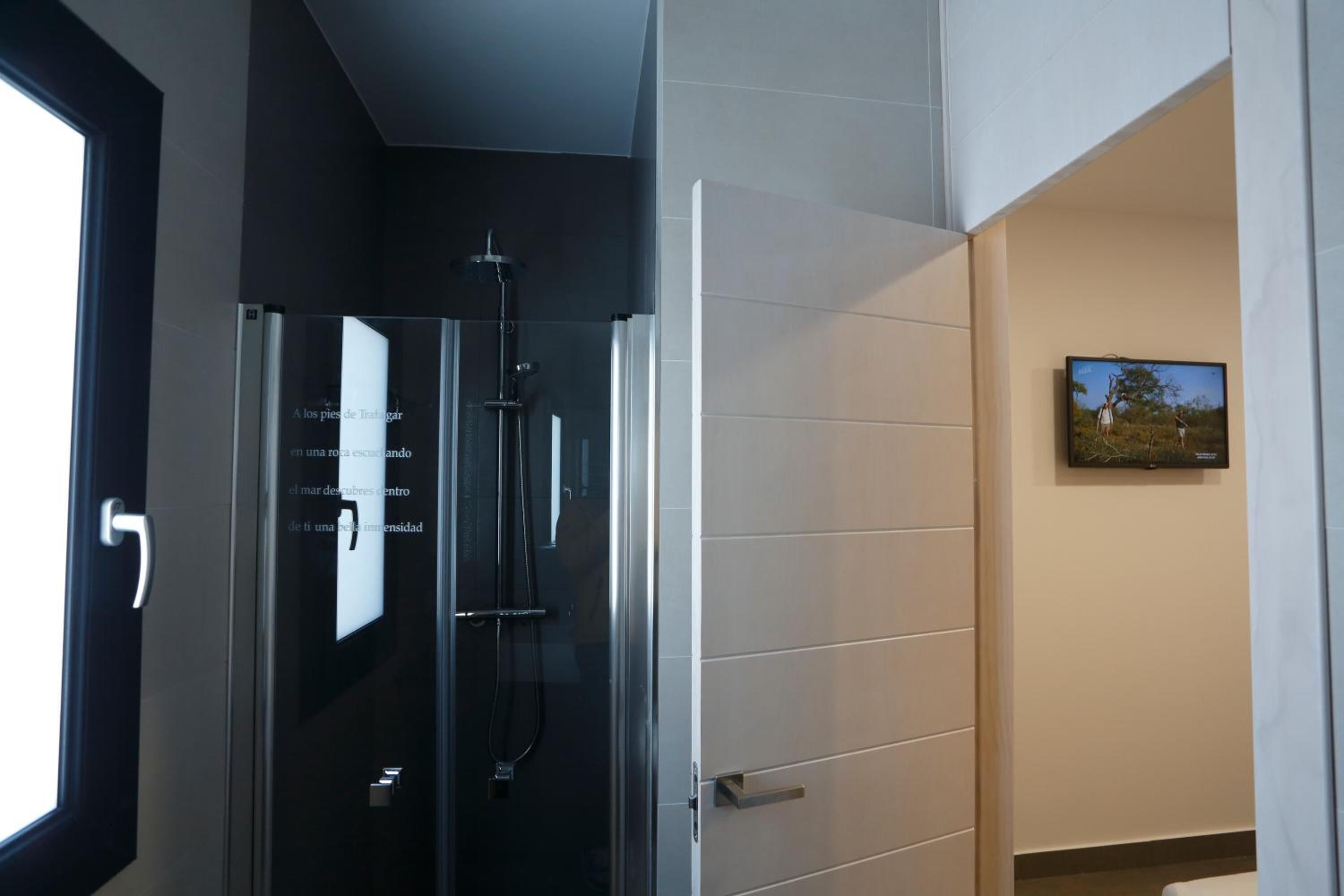 A modern bathroom with a glass shower enclosure, a white tiled wall, and a framed picture on the wall.