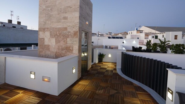 Una terraza en la azotea con piso de madera, un muro de piedra y un ventanal que da a un espacio interior.