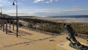 Un paseo marítimo con una estatua, un muro de piedra y vistas a la playa y al océano.
