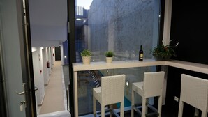Un interior moderno con un separador de vidrio, sillas de mimbre blanco y una pequeña mesa con plantas en macetas y copas de vino.