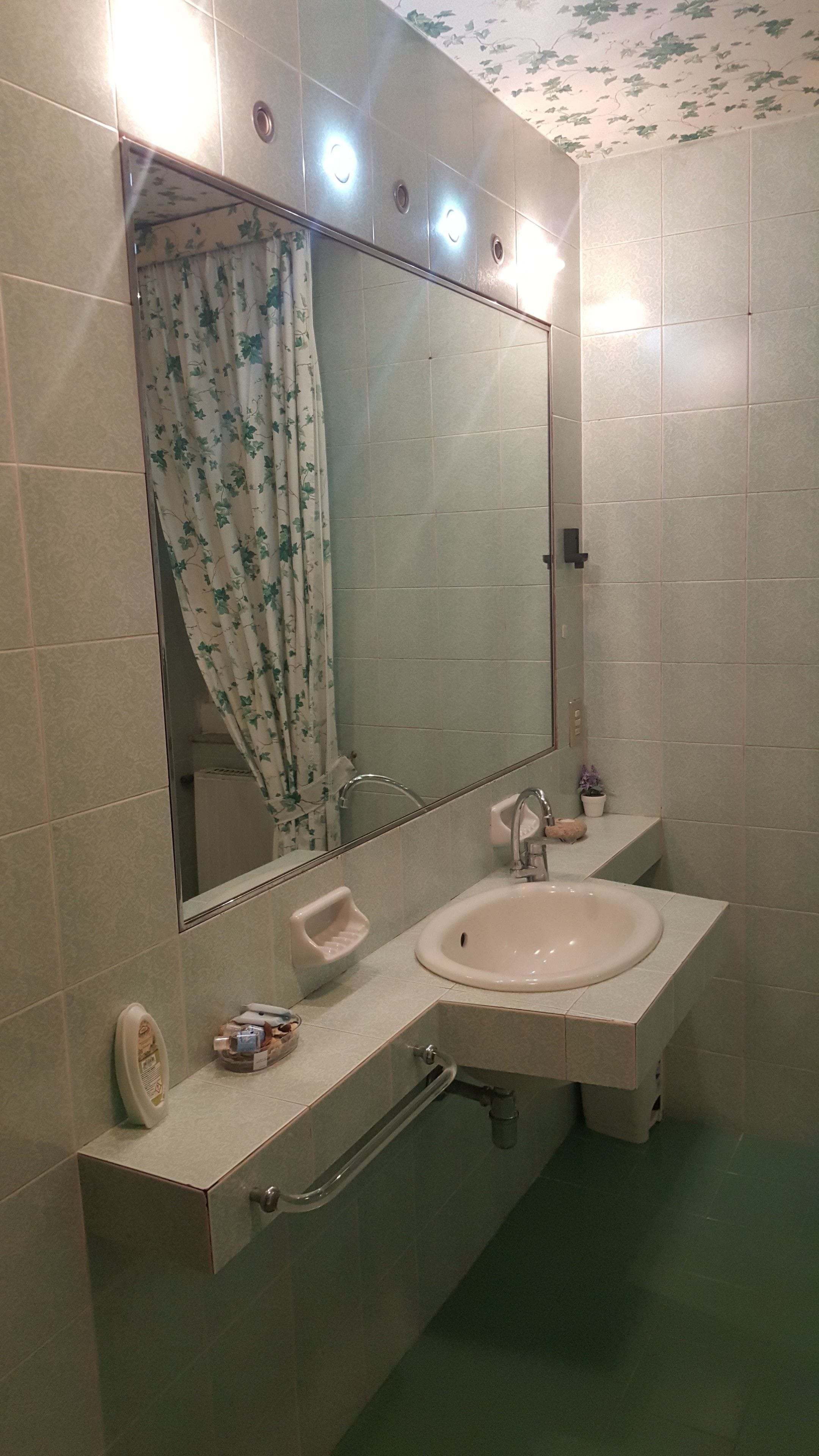 A bathroom with a large mirror, a sink, and a shower curtain with a floral pattern.