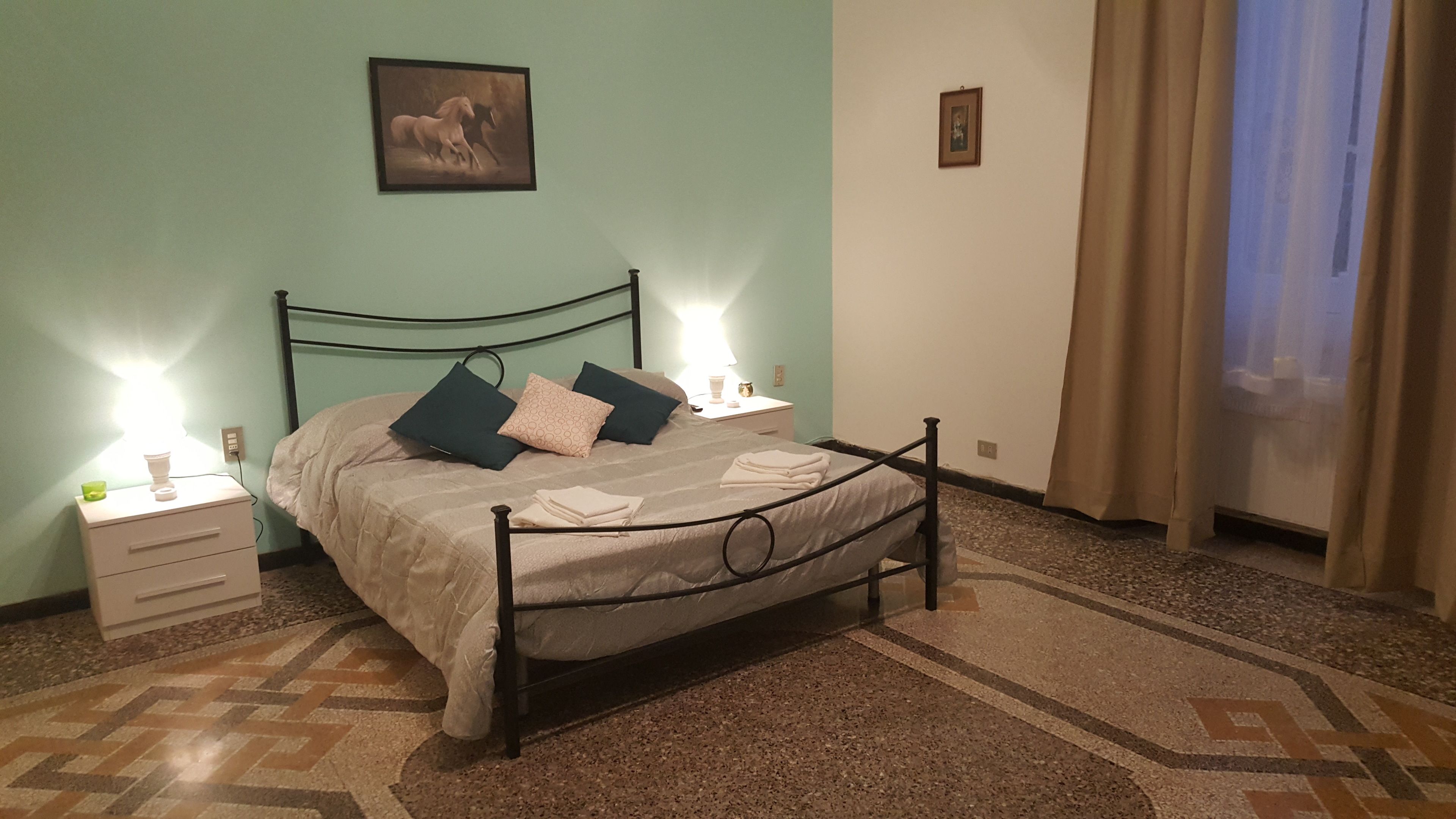Una camera da letto con un letto, comodini, una lampada, un quadro e un pavimento decorato.