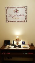 A hotel room with a 'Royal Suite' sign, a lamp with a photo, a phone, a WiFi sign, and a small table with snacks and a tissue box.